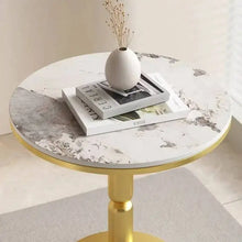 Round marble table with gold base, books, and a vase on a light background